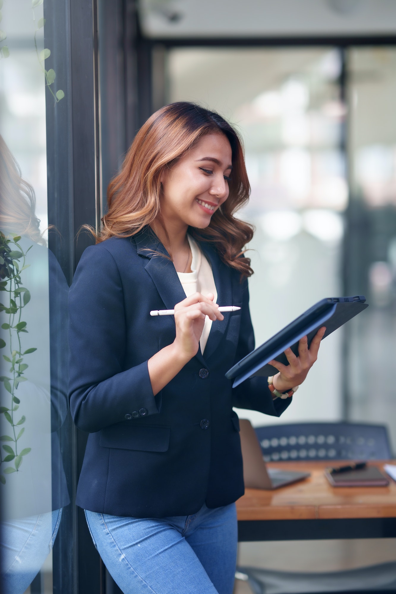 Attractive smiling Asian businesswoman standing holding tablet working and recording work details