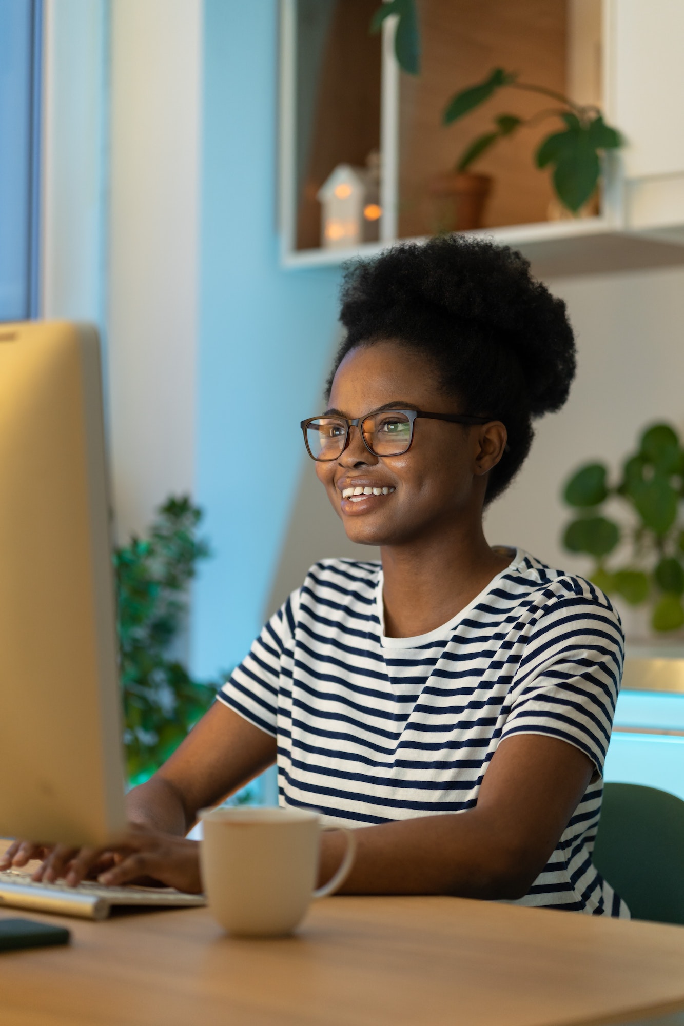 Happy young African woman remote worker looking at computer monitor with smile, working remotely