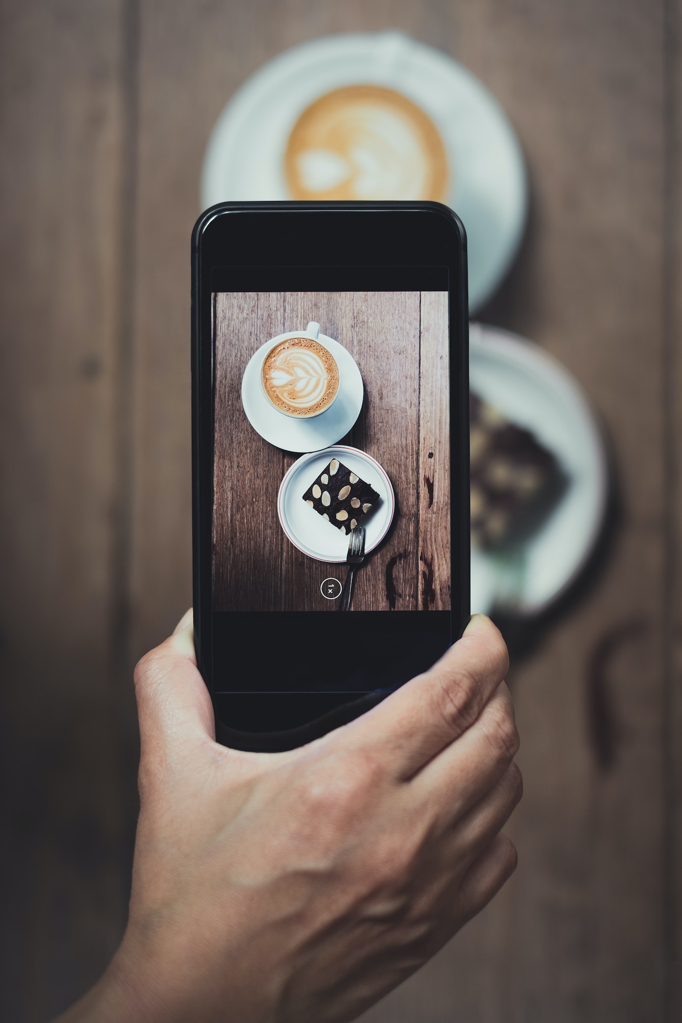 Top view of Hand holding mobile take a photo of coffee cup and cake