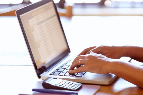 Calculating her tax for the month. Closeup detail view of female hands using a laptop.