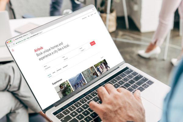 cropped shot of young businessman using laptop with airbnb website on screen