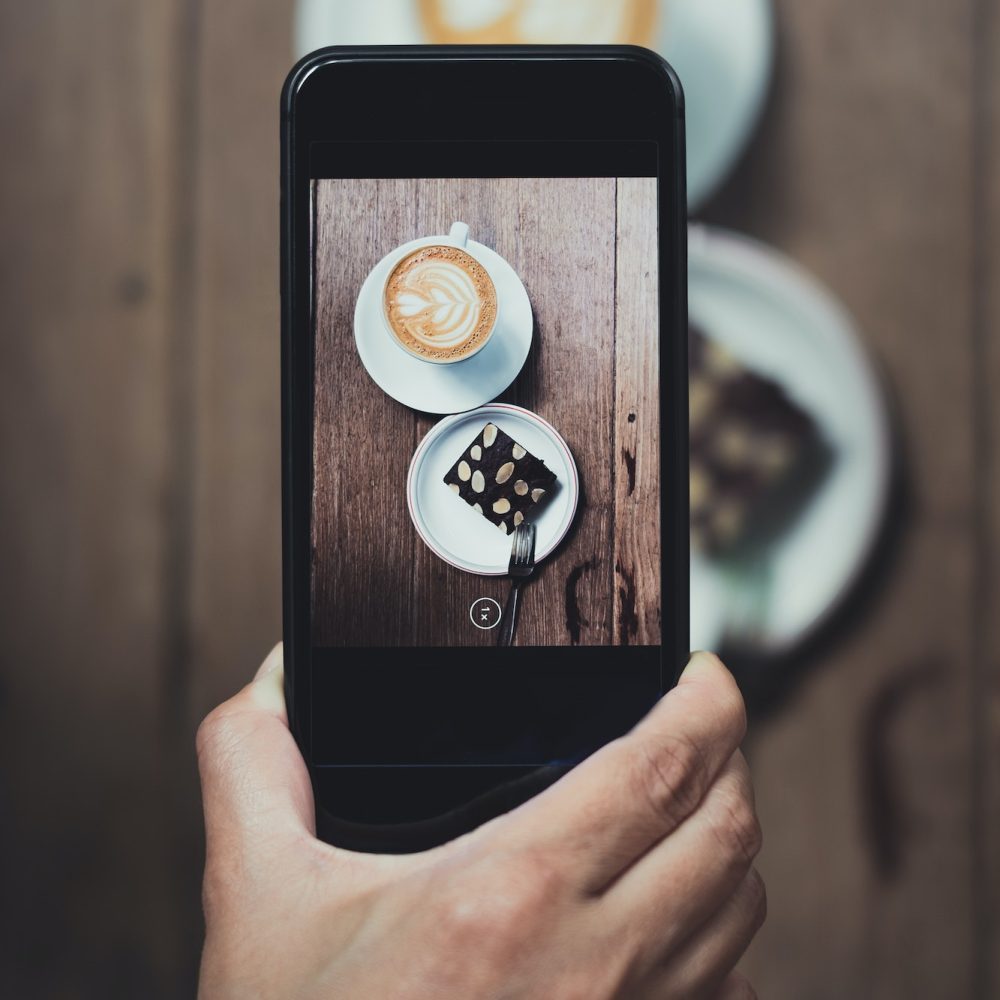 Top view of Hand holding mobile take a photo of coffee cup and cake